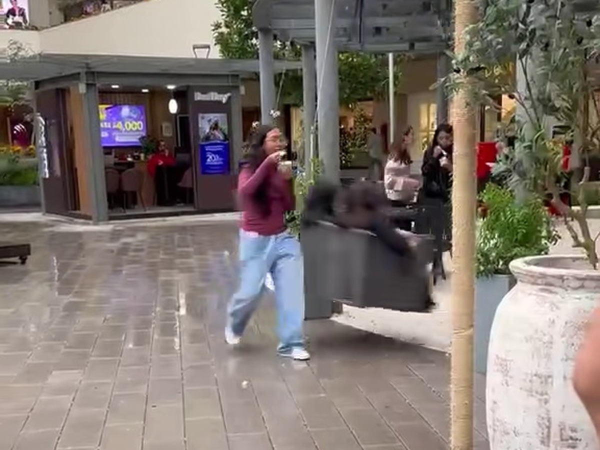 Una joven camina con un helado por el pasillo de un centro comercial mientras un columpio se acerca por detrás