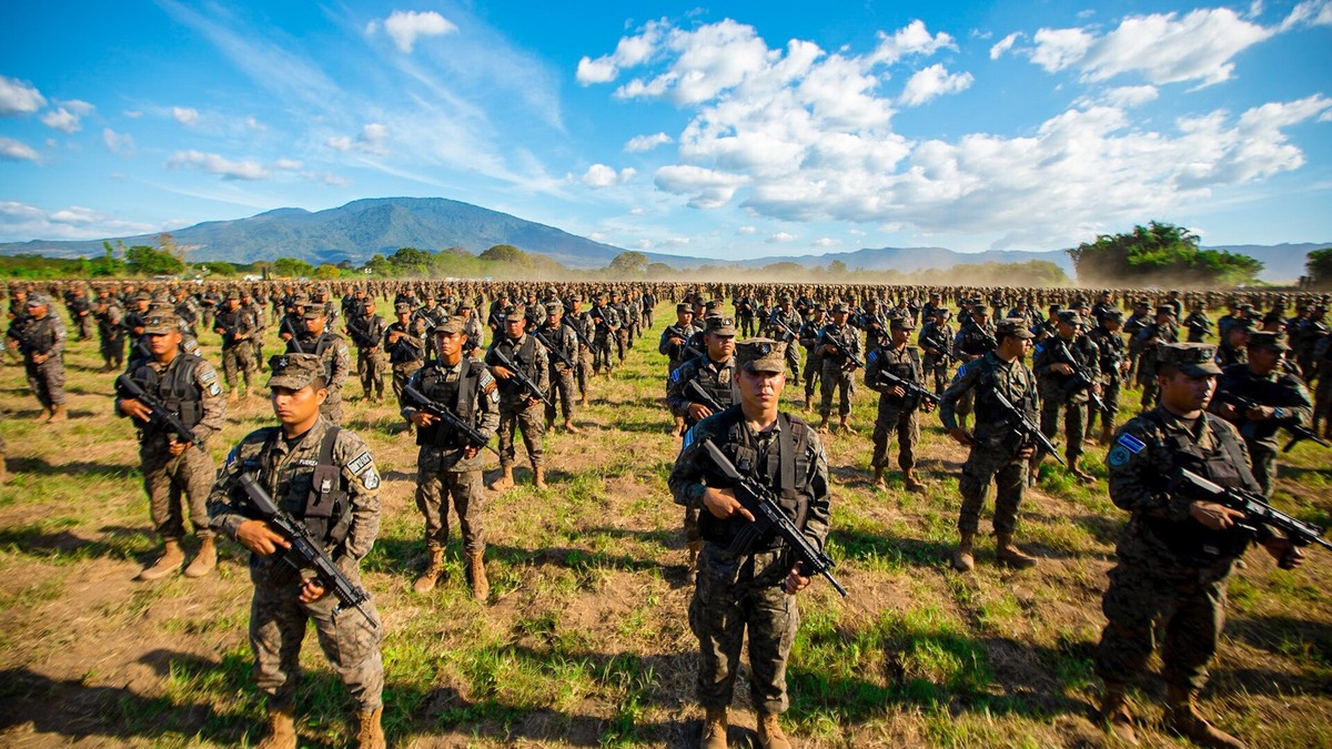 Soldados de la Fuerza Armada de El Salvador en formación con sus fusiles, en un campo al pie de un volcán