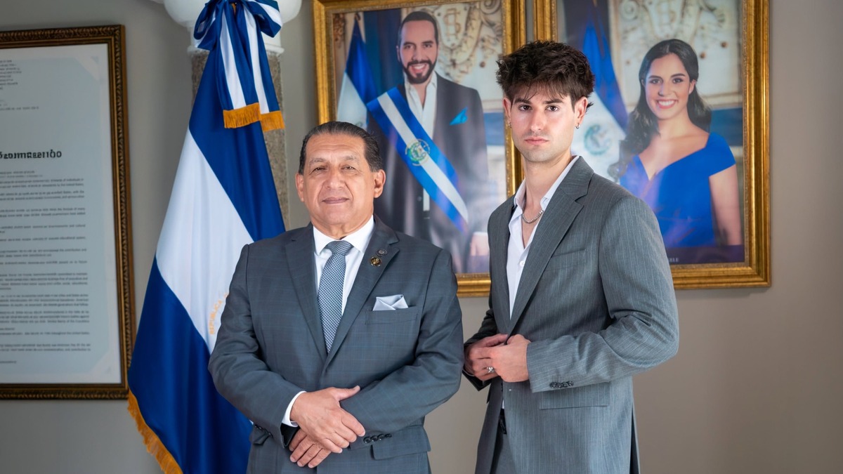 Juanfer Sendra, de traje, junto a un funcionario bajo los retratos del presidente Nayib Bukele y la primera dama