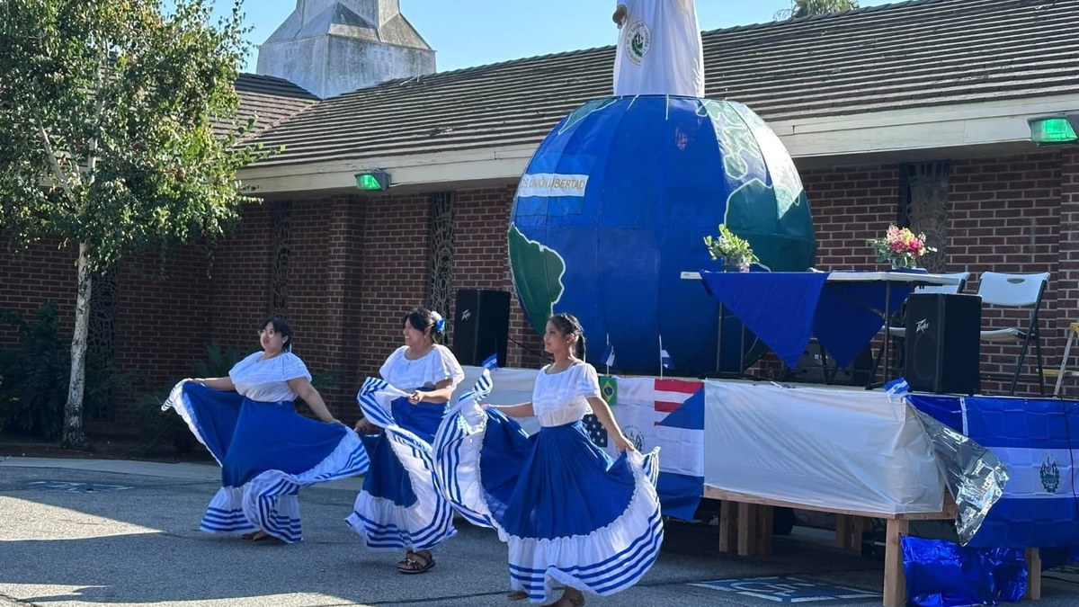 Bailarinas de danza folklórica con trajes azules y blancos frente a una carroza con la imagen del Divino Salvador del Mundo