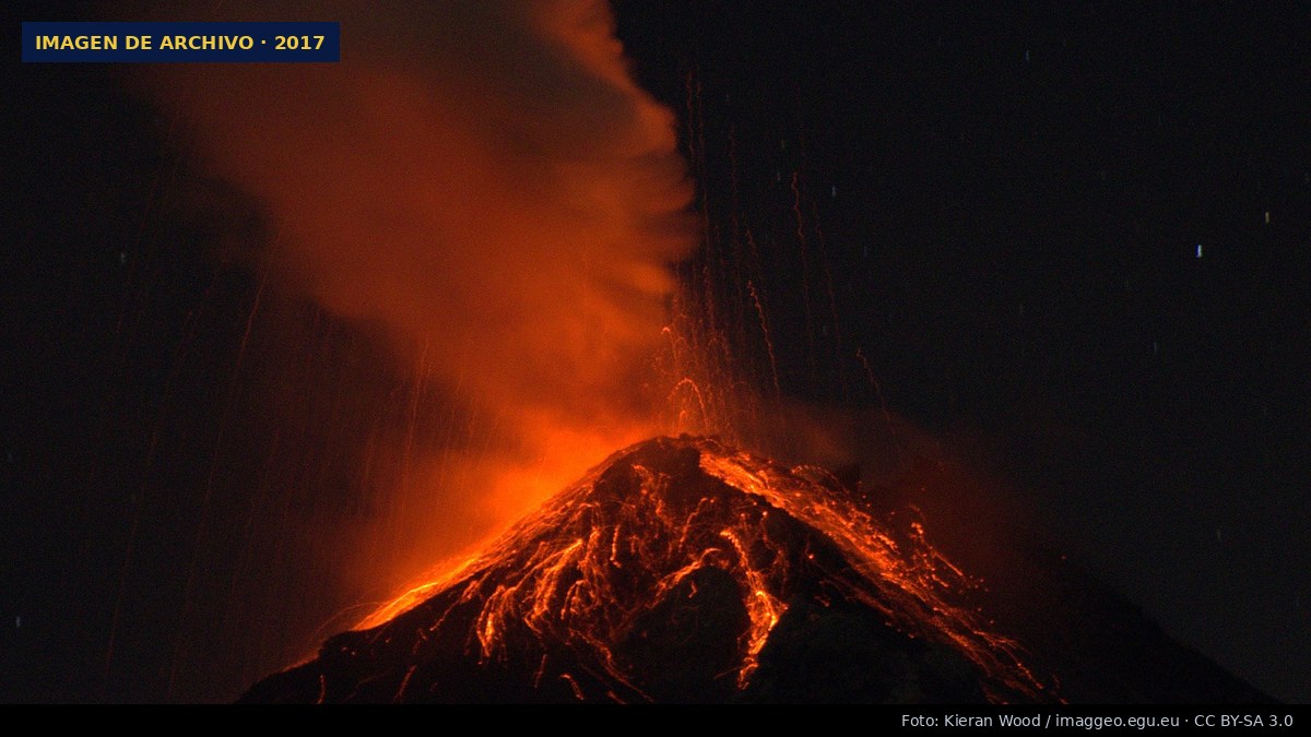 El volcán de Fuego en erupción durante la noche, con lava incandescente bajando por sus laderas y una columna de ceniza