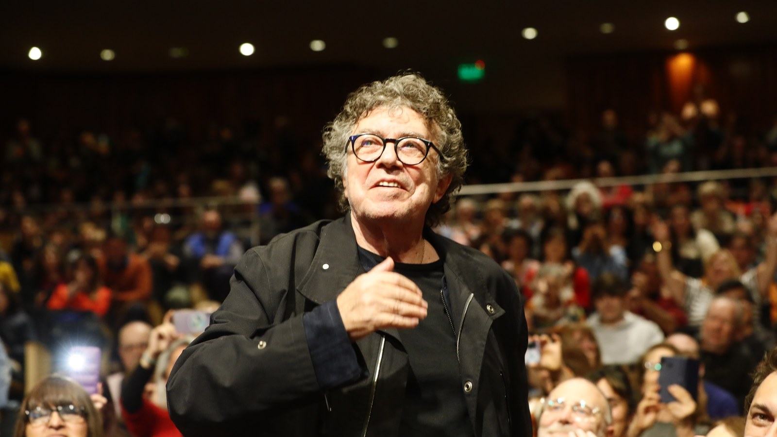 Piero saluda al público, con la mano en el pecho, en un auditorio lleno